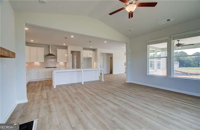 kitchen with white cabinets, decorative backsplash, a kitchen island with sink, and wall chimney range hood