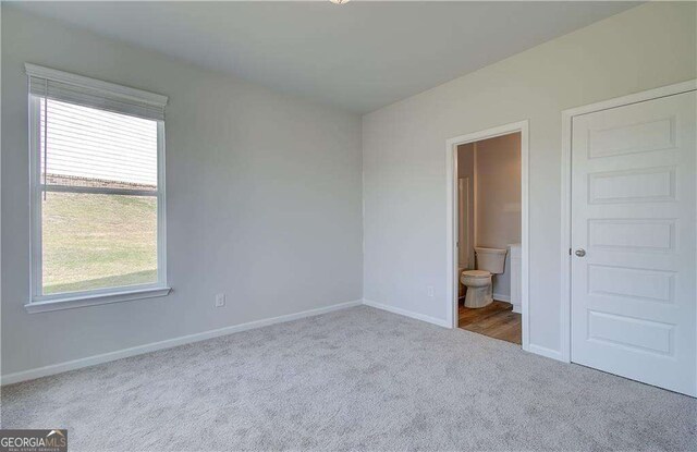 unfurnished bedroom featuring ensuite bathroom and light carpet