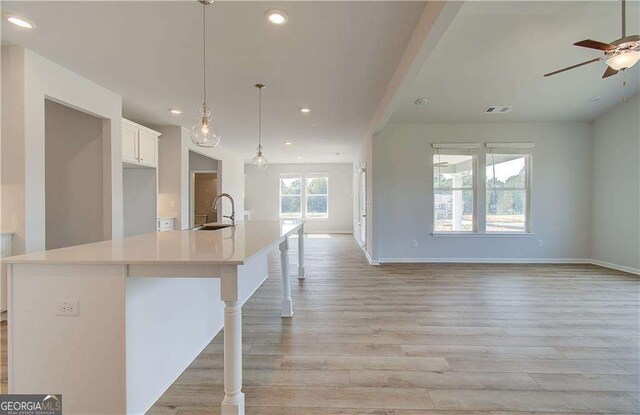 kitchen with sink, a kitchen breakfast bar, a large island with sink, decorative light fixtures, and white cabinets