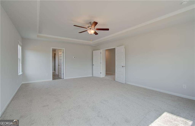 unfurnished bedroom featuring ceiling fan, light carpet, and a tray ceiling