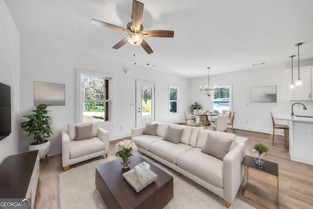 living room featuring light wood-type flooring, ceiling fan with notable chandelier, plenty of natural light, and sink