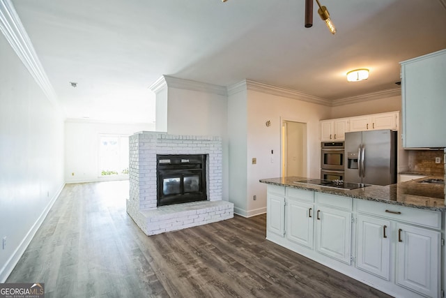 kitchen featuring white cabinetry, stainless steel appliances, dark stone countertops, ornamental molding, and a brick fireplace