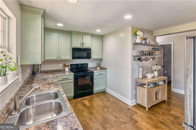 kitchen with black appliances, green cabinetry, sink, and wood-type flooring