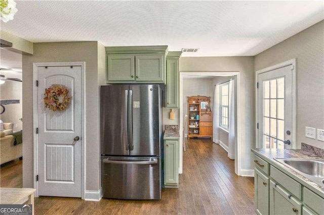 kitchen with wood-type flooring, stainless steel refrigerator, ceiling fan, green cabinets, and sink