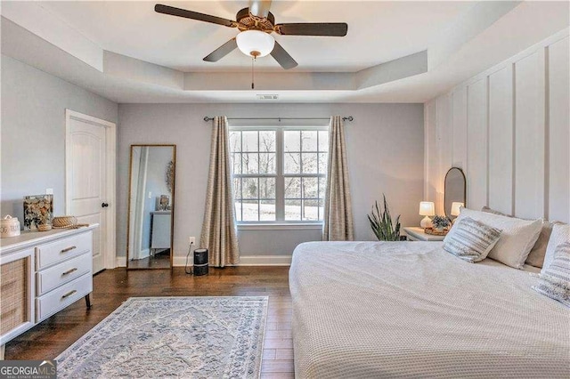 bedroom with ceiling fan, a raised ceiling, and dark hardwood / wood-style floors