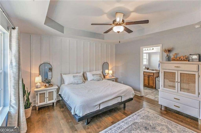 bedroom featuring a tray ceiling, ceiling fan, dark hardwood / wood-style flooring, and ensuite bathroom