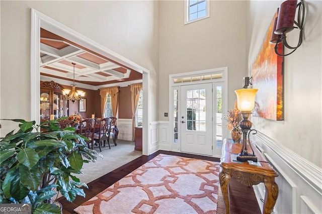 foyer featuring an inviting chandelier, coffered ceiling, crown molding, dark hardwood / wood-style floors, and beam ceiling