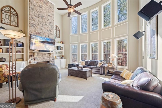 living room with a stone fireplace, ceiling fan, built in features, a towering ceiling, and carpet floors