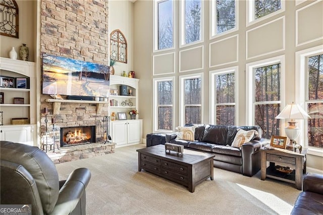 living room featuring built in shelves, a fireplace, a towering ceiling, and light colored carpet