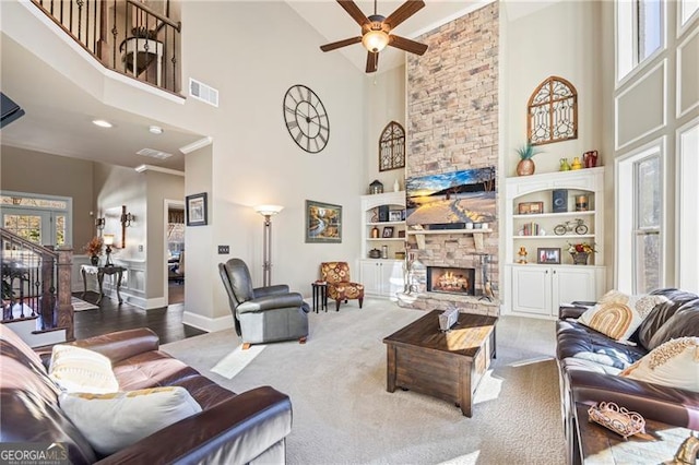 living room featuring a stone fireplace, crown molding, ceiling fan, a towering ceiling, and carpet floors