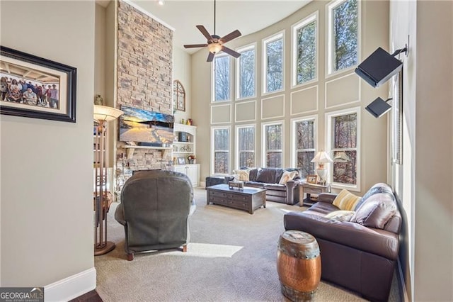 carpeted living room with a stone fireplace, ceiling fan, and a towering ceiling