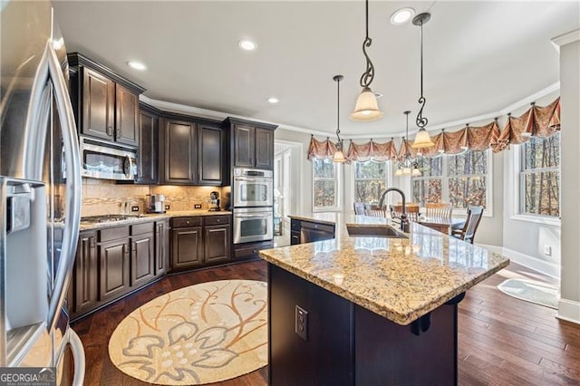 kitchen with sink, hanging light fixtures, an island with sink, appliances with stainless steel finishes, and ornamental molding