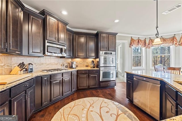 kitchen with tasteful backsplash, pendant lighting, dark brown cabinets, appliances with stainless steel finishes, and ornamental molding