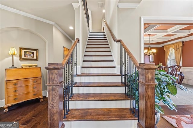 stairs featuring beam ceiling, coffered ceiling, crown molding, a chandelier, and wood-type flooring