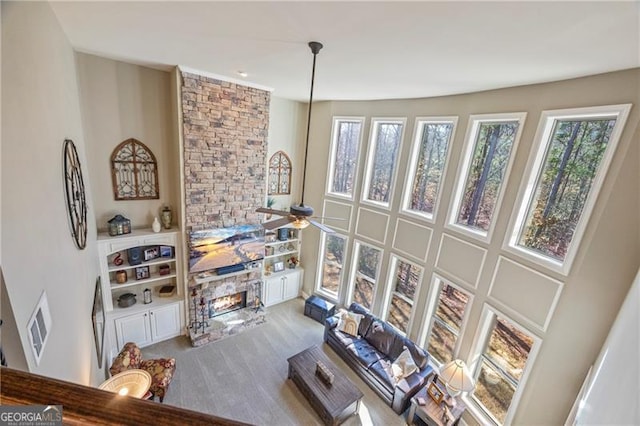 carpeted living room featuring a stone fireplace and ceiling fan