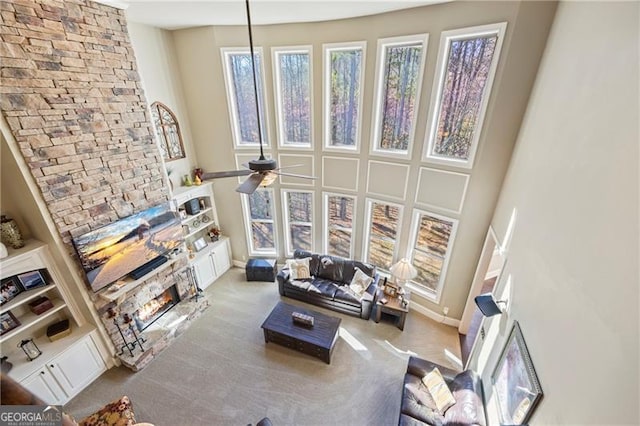 living room featuring ceiling fan, a fireplace, light carpet, and a high ceiling