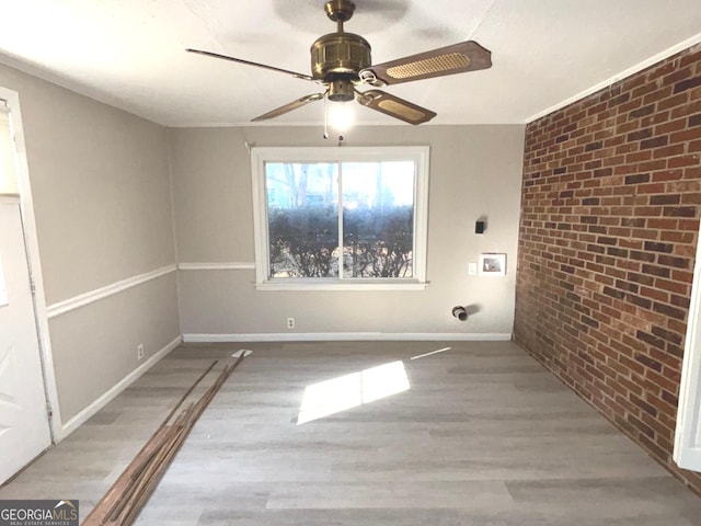 empty room with light wood-type flooring, ceiling fan, and brick wall