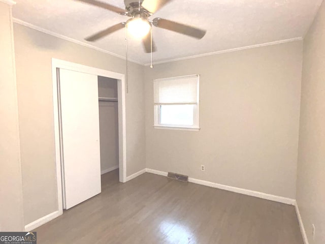 unfurnished bedroom with hardwood / wood-style floors, ceiling fan, crown molding, and a closet