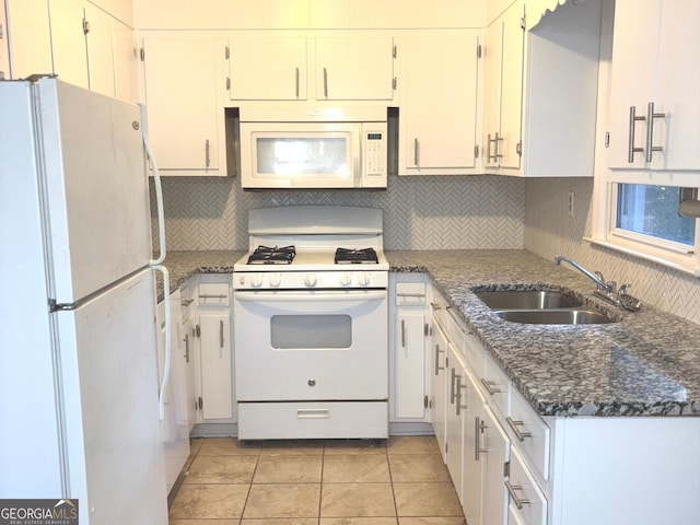 kitchen with sink, light tile patterned flooring, dark stone counters, white appliances, and white cabinets