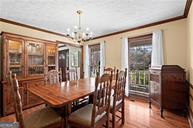 dining area with light hardwood / wood-style flooring, a chandelier, a textured ceiling, and ornamental molding