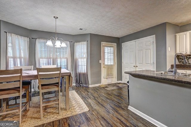 dining space featuring a textured ceiling, sink, dark wood-type flooring, and a chandelier