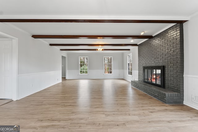 unfurnished living room featuring beam ceiling, light hardwood / wood-style floors, ornamental molding, and a fireplace