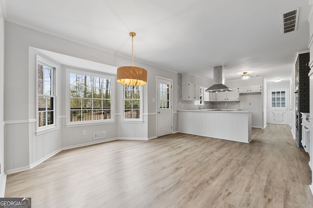 kitchen featuring white cabinets, light wood-type flooring, tasteful backsplash, island range hood, and kitchen peninsula