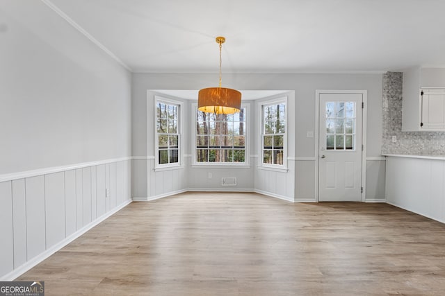 unfurnished dining area featuring light hardwood / wood-style floors, an inviting chandelier, and crown molding