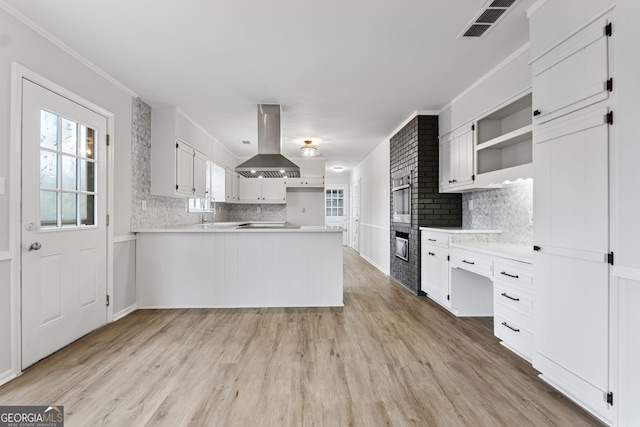 kitchen featuring white cabinets, island range hood, kitchen peninsula, and ornamental molding