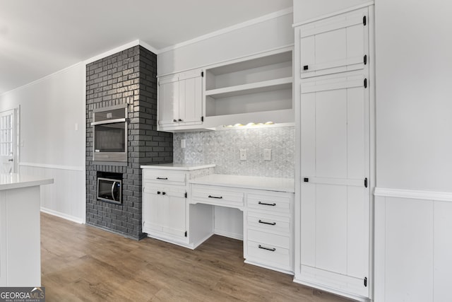 kitchen featuring crown molding, oven, wood-type flooring, a fireplace, and white cabinets