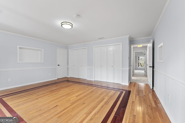 unfurnished bedroom featuring multiple closets, ornamental molding, and light hardwood / wood-style flooring