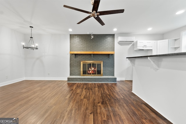 unfurnished living room featuring a fireplace, ceiling fan with notable chandelier, a wall unit AC, and dark wood-type flooring