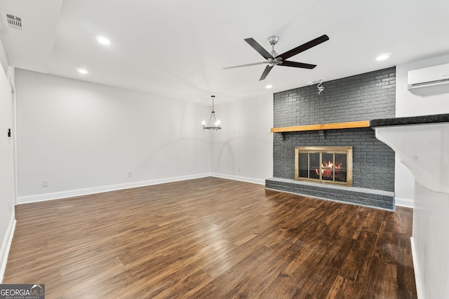 unfurnished living room with ceiling fan with notable chandelier, a fireplace, a wall mounted air conditioner, and dark hardwood / wood-style floors