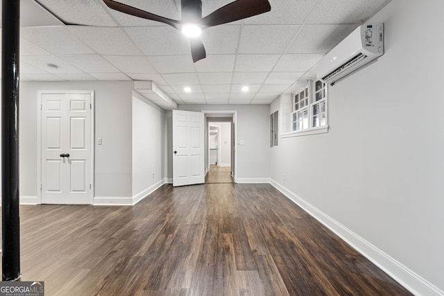 basement with a wall mounted AC, ceiling fan, and dark hardwood / wood-style floors