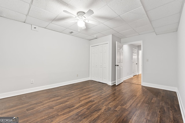 spare room with a drop ceiling, ceiling fan, and dark wood-type flooring