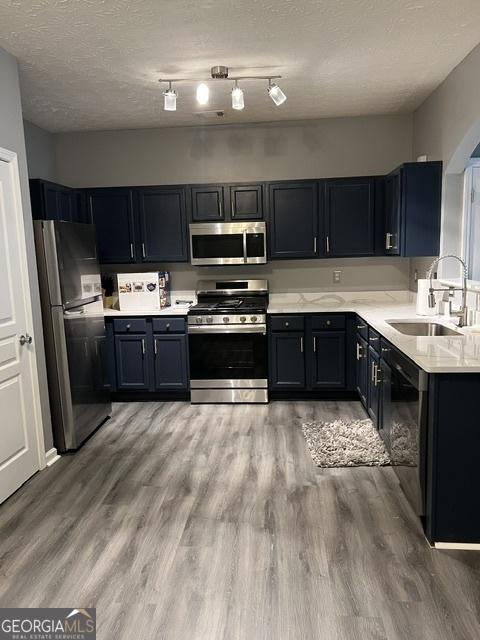 kitchen with a textured ceiling, sink, wood-type flooring, and stainless steel appliances