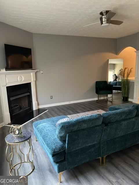 living room with ceiling fan, dark hardwood / wood-style flooring, and a textured ceiling