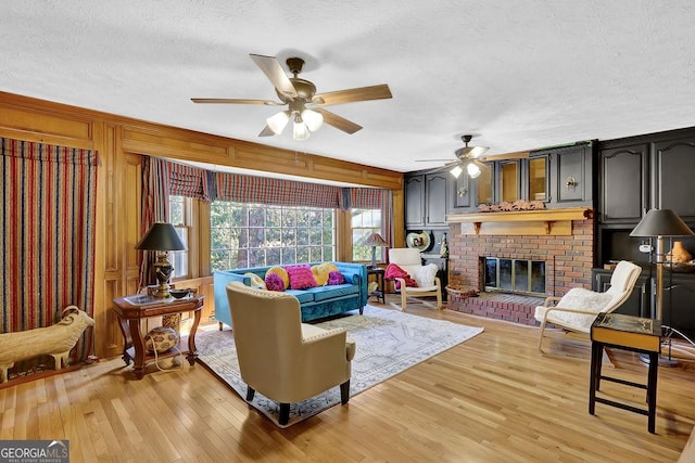 living room featuring ceiling fan, a fireplace, light hardwood / wood-style floors, and a textured ceiling