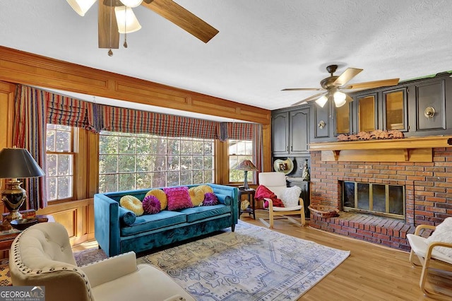 living room featuring ceiling fan, light hardwood / wood-style floors, a textured ceiling, and a brick fireplace