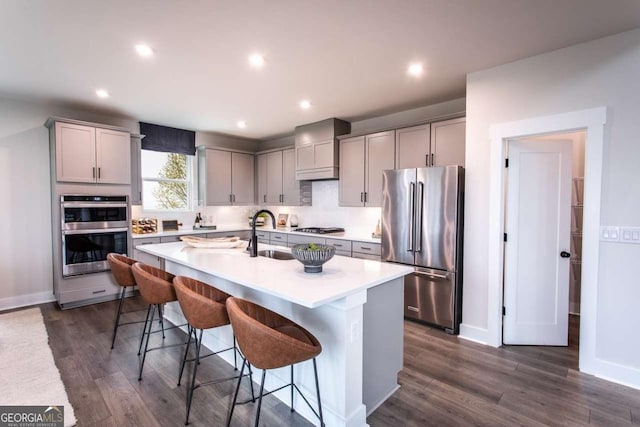 kitchen featuring a breakfast bar, stainless steel appliances, a kitchen island with sink, and gray cabinetry