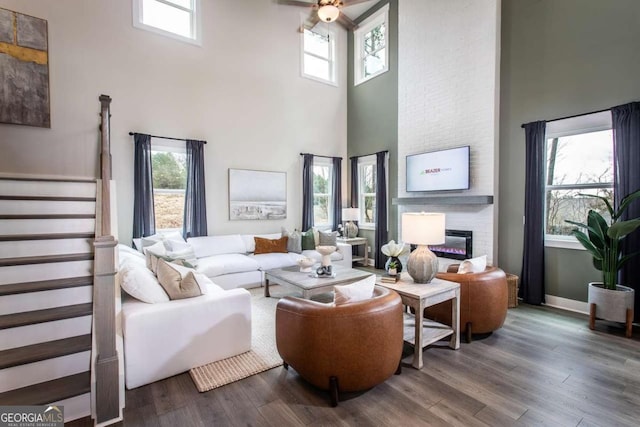 living room with hardwood / wood-style floors, ceiling fan, a large fireplace, and a high ceiling