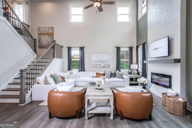 living room with a high ceiling, a brick fireplace, a wealth of natural light, and hardwood / wood-style floors