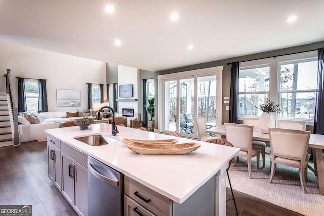 kitchen featuring stainless steel dishwasher, a wealth of natural light, gray cabinetry, sink, and an island with sink