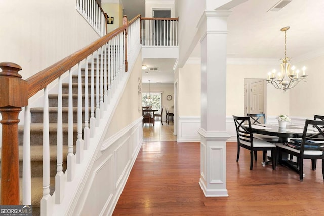 foyer entrance featuring hardwood / wood-style floors, an inviting chandelier, ornamental molding, and ornate columns