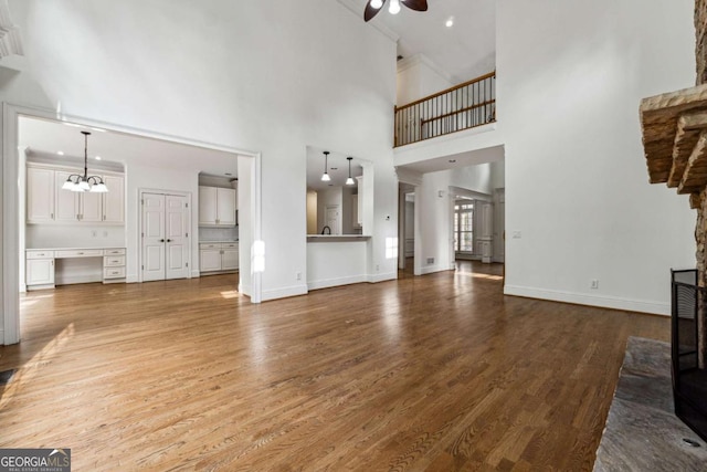 unfurnished living room with ceiling fan with notable chandelier, wood-type flooring, and a towering ceiling