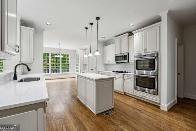 kitchen with hanging light fixtures, sink, appliances with stainless steel finishes, a kitchen island, and white cabinetry