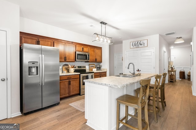 kitchen featuring sink, stainless steel appliances, decorative light fixtures, a kitchen island with sink, and a breakfast bar