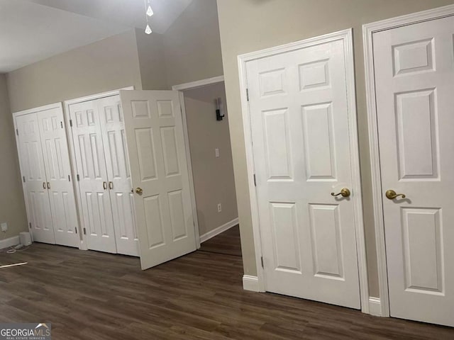 unfurnished bedroom with dark wood-type flooring, vaulted ceiling, and multiple closets