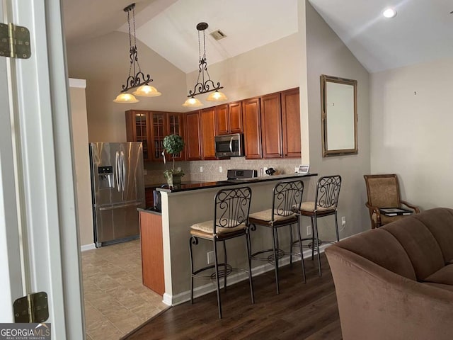 kitchen with pendant lighting, a breakfast bar, appliances with stainless steel finishes, tasteful backsplash, and kitchen peninsula