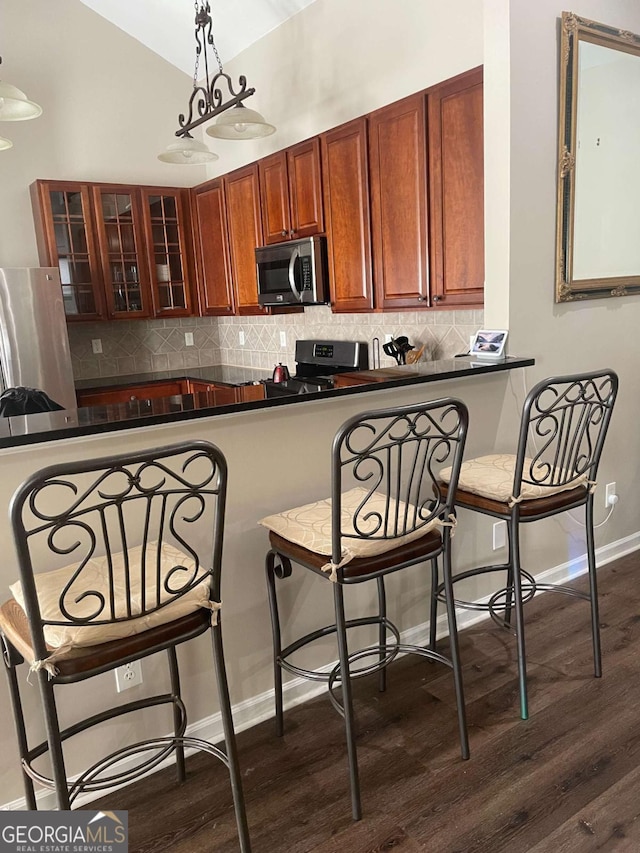 kitchen featuring stainless steel appliances, kitchen peninsula, decorative light fixtures, vaulted ceiling, and a breakfast bar area